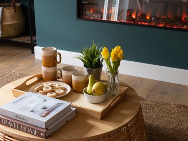 A wooden coffee table with a tray holding mugs, cookies, pears, a plant, and yellow flowers near a fireplace at Hebog in Beddgelert