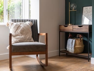 A chair with a decorative cushion and a wooden side table with drawers holding a basket and lamp at Hebog in Beddgelert