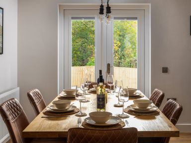 A dining table set with plates bowls wine glasses and bottles in a room with glass doors at Hebog in Beddgelert