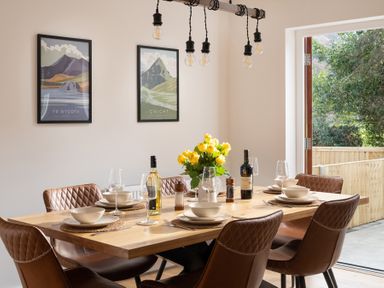 A dining room with a wooden table set with plates bowls wine glasses two bottles of wine salt and pepper shakers and yellow flowers in a vase at Hebog in Beddgelert