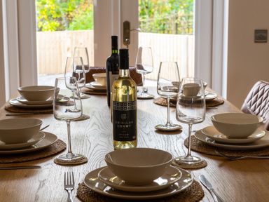 A dining table set with bowls plates wine glasses and two bottles of wine at Hebog in Beddgelert