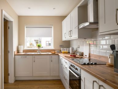 A kitchen with white cabinets wooden countertops a sink under a window a stove and various kitchen appliances at Hebog in Beddgelert