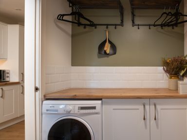 A laundry area with a washing machine under a wooden countertop and a drying brush set hanging on the wall at Hebog in Beddgelert