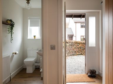 A small toilet room with a toilet and sink next to an open front door with a doormat and a pair of boots visible at Hebog in Beddgelert