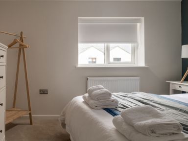 A bedroom with folded towels on a bed near a window beside a wooden clothes rack at Hebog in Beddgelert
