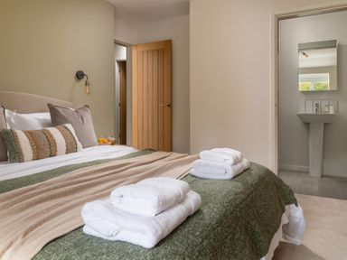 A bedroom with a bed made with green and beige blankets folded towels on the bed an open door leading to a bathroom with a sink and mirror at Hebog in Beddgelert
