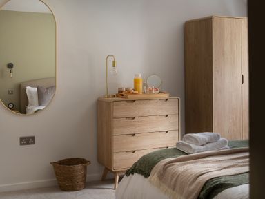 A bedroom with a wooden dresser holding a tray with breakfast items next to a wooden wardrobe and a bed with folded towels at Hebog in Beddgelert