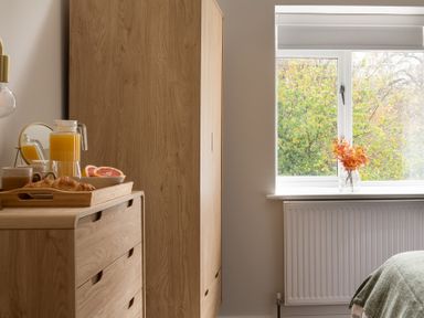 A wooden dresser with a tray of breakfast items next to a wardrobe and a window with a vase of orange flowers at Hebog in Beddgelert
