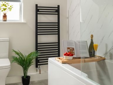 A bathroom with a white toilet a black towel radiator a potted plant and a bathtub with a wooden tray holding a book bowl of strawberries bottle and glass of orange juice at Hebog in Beddgelert
