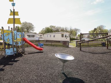 A playground with a slide and climbing equipment next to mobile homes at The Maples in Steel Green near Haverigg