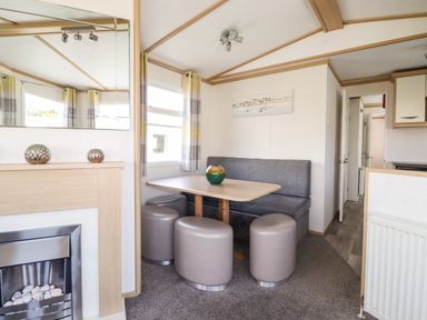 A dining area with a table surrounded by stools and a bench next to a fireplace at The Maples in Steel Green near Haverigg