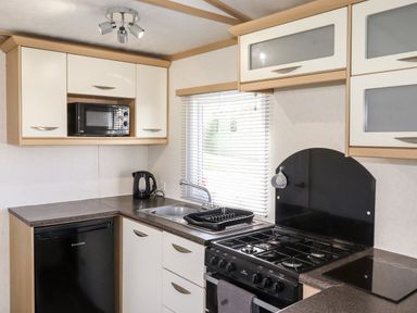 A kitchen with cabinets a microwave a kettle a sink a drying rack a window and a stove at The Maples in Steel Green near Haverigg