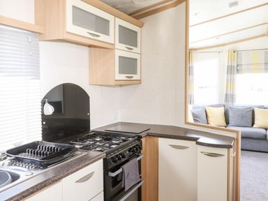 A kitchen with stove and countertops next to a living room with sofa and cushions at The Maples Steel Green near Haverigg