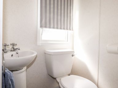A bathroom with a toilet sink window and striped blind at The Maples in Steel Green near Haverigg