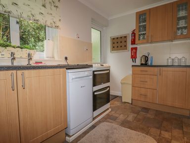 A kitchen with wooden cabinets dishwasher stove kettle fire extinguisher and storage containers at Merryfield Lodge Rosecraddoc near Liskeard