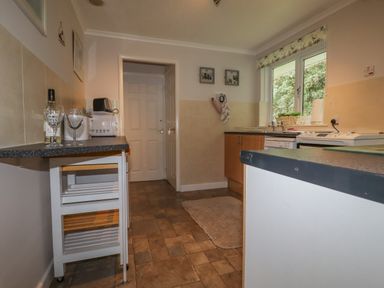 A kitchen with a countertop wine bottle and glasses a microwave and toaster a window above the sink and cabinets at Merryfield Lodge Rosecraddoc near Liskeard