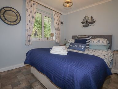 A bedroom with a double bed covered in blue bedding and nautical themed pillows and curtains at Merryfield Lodge in Rosecraddoc near Liskeard