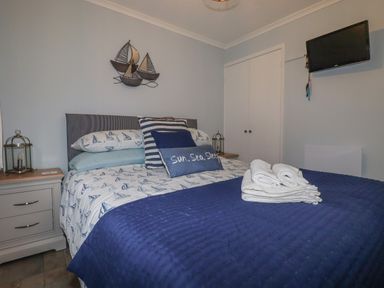A bedroom with a double bed towels on the bed nightstands with lamps wall decor and a wall-mounted TV at Merryfield Lodge in Rosecraddoc near Liskeard