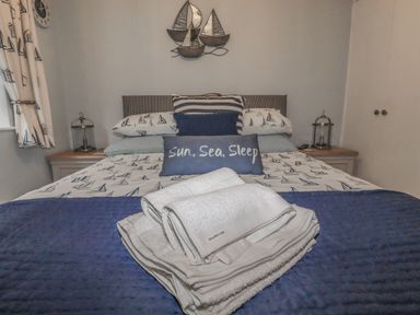 A bedroom with a bed with sailboat-themed bedding and pillows and folded white towels on a blue blanket at Merryfield Lodge Rosecraddoc near Liskeard
