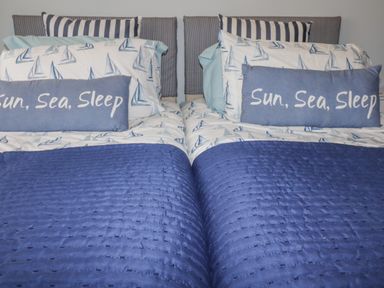A bedroom with two single beds with blue boat patterned bedding and blue cushions with text at Merryfield Lodge in Rosecraddoc near Liskeard