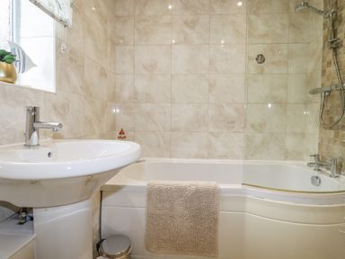 A bathroom with a sink a bathtub with a shower and beige tiles at Merryfield Lodge Rosecraddoc near Liskeard
