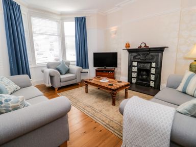 A living room with blue curtains a wooden coffee table a television and a black fireplace at 3 St Davids Place in Llandudno