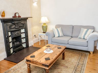 A living room with a grey sofa and striped cushions a wooden coffee table and a fireplace at 3 St Davids Place in Llandudno