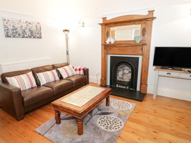 A living room with a brown leather sofa striped pillows wooden coffee table rug and fireplace at 3 St Davids Place in Llandudno