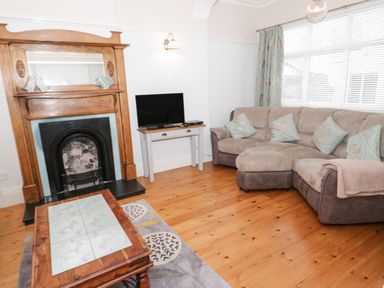 A living room with a wooden fireplace a television on a stand a sectional sofa with cushions and a wooden coffee table at 3 St Davids Place in Llandudno