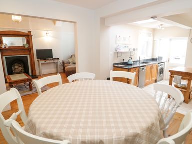 A dining area with a round table and chairs adjacent to a kitchen with wooden cabinets and appliances at 3 St Davids Place in Llandudno