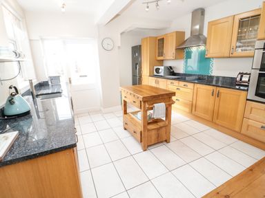 A kitchen with wooden cabinets a small wooden island a refrigerator a microwave and a kettle at 3 St Davids Place in Llandudno