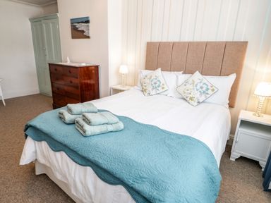 A bedroom with a made bed with blue blanket and towels on it a wooden dresser green wardrobe and two bedside tables with lamps at 3 St Davids Place in Llandudno