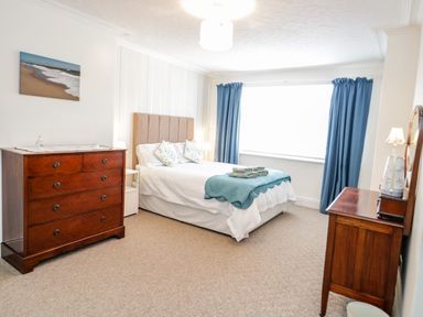 A bedroom with a double bed blue curtains wooden dressers and a beach painting at 3 St Davids Place Llandudno