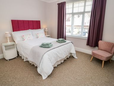 A bedroom with a double bed with folded towels bedside tables lamps a window with curtains and a pink chair at 3 St Davids Place in Llandudno
