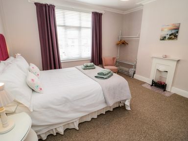 A bedroom with a bed folded towels purple curtains a small chair and a white decorative fireplace at 3 St Davids Place in Llandudno