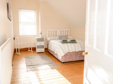 A bedroom with a bed white headboard towels on the bed bedside table lamp striped rug wooden floor at 3 St Davids Place in Llandudno
