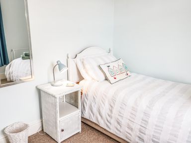 A bedroom with a single bed with striped bedding a bedside table with a lamp a mirror and a wastebasket at 3 St. Davids Place in Llandudno