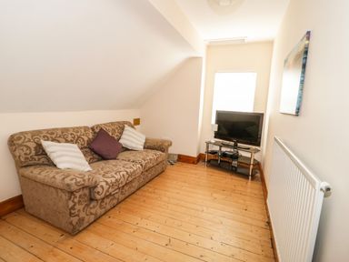 A small living room with a patterned sofa with cushions a television on a stand a radiator and a window at 3 St Davids Place in Llandudno