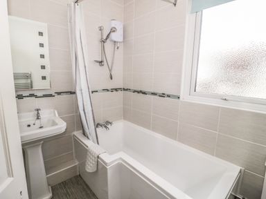 A bathroom with a bathtub shower combination sink and a frosted window at 3 St Davids Place in Llandudno