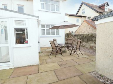 A patio area with a glass table four chairs and a large umbrella at 3 St Davids Place in Llandudno