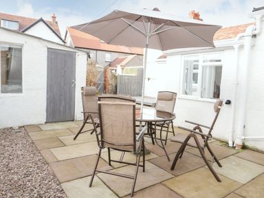 An outdoor patio area with a round glass table, four chairs, and a large umbrella at 3 St Davids Place in Llandudno