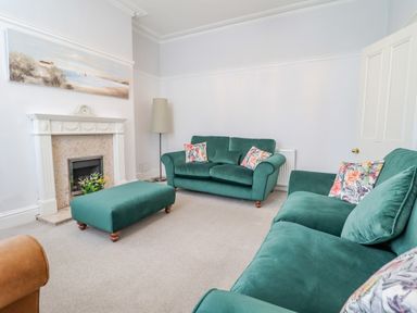 A living room with green sofas a green ottoman a fireplace and a floor lamp at 24 Cadnant Park in Conwy