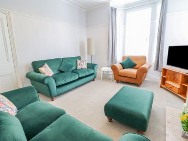 A living room with green sofas a brown armchair a wooden TV stand and grey curtains at 24 Cadnant Park in Conwy