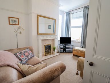A living room with a fireplace a sofa a TV on a glass stand and blue curtains at 24 Cadnant Park in Conwy