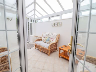 A sunroom with wicker furniture including a loveseat and chair a wooden side table and small stools at 24 Cadnant Park in Conwy