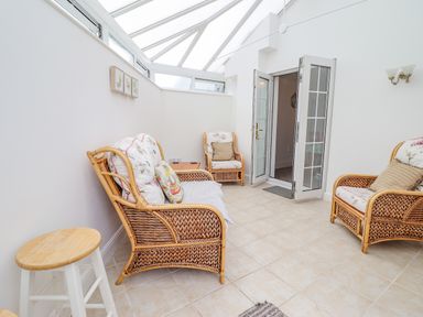 A conservatory with wicker furniture and floral cushions at 24 Cadnant Park in Conwy