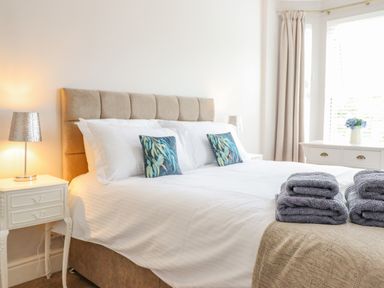 A bedroom with a bed with white bedding and decorative pillows beside bedside tables with lamps at 24 Cadnant Park in Conwy