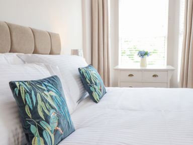 A bedroom with a bed featuring decorative cushions and a dresser with a vase of flowers at 24 Cadnant Park in Conwy