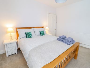 A bedroom with a wooden bed frame white bedding blue towels on the bed two bedside tables with lamps at 24 Cadnant Park in Conwy