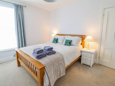 A bedroom with a wooden bed frame with folded towels on the bed and a bedside table with a lamp at 24 Cadnant Park in Conwy